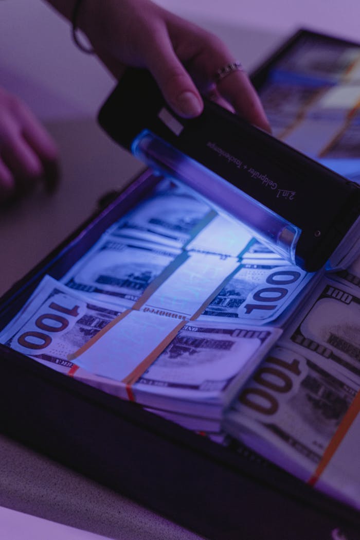 A person using a UV light to verify bundles of 100 dollar bills in an attache case.